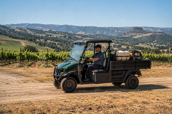 A commercial utility vehicle with a cargo bed loaded with equipment, being driven across a large commercial or agricultural property in California.