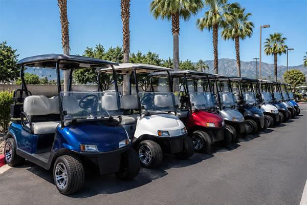 A row of clean, refurbished golf cars displayed in an outdoor dealership lot under bright California sunshine.